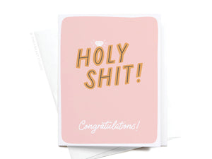 The Holy Shit Engagement Ring Greeting Card by Onderkast Studio features a pink background, bold gold “HOLY SHIT!” lettering, a diamond illustration, and “Congratulations!” in white script—perfect for engagements.